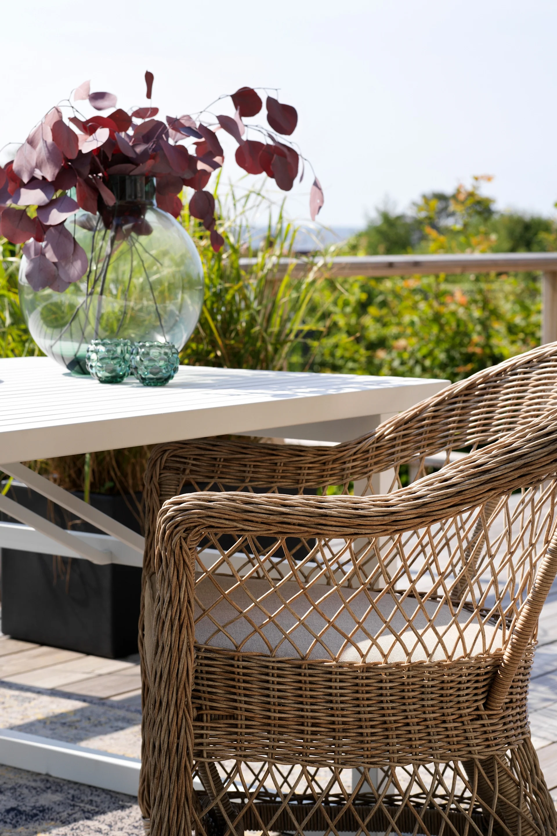 La chaise à accoudoirs Kamomill de Brafab est posée sur une terrasse, à côté d'une table.