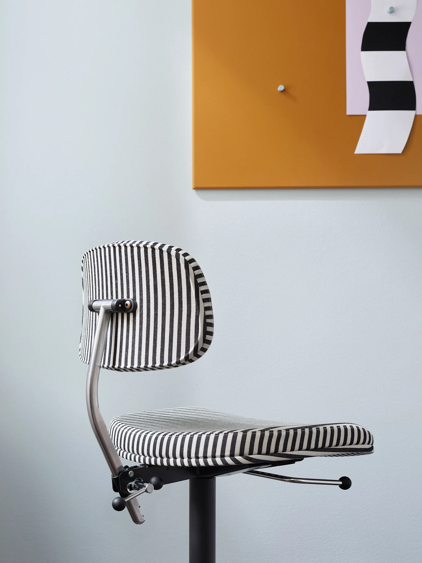 Un fauteuil de bureau moderne à rayures verticales noires et blanches, devant un mur bleu clair et un tableau orange.