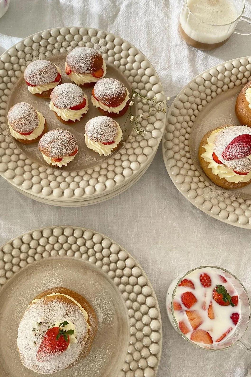 Brioches à la crème avec crème fouettée, fraises et sucre glace sur des assiettes texturées, avec des boissons.
