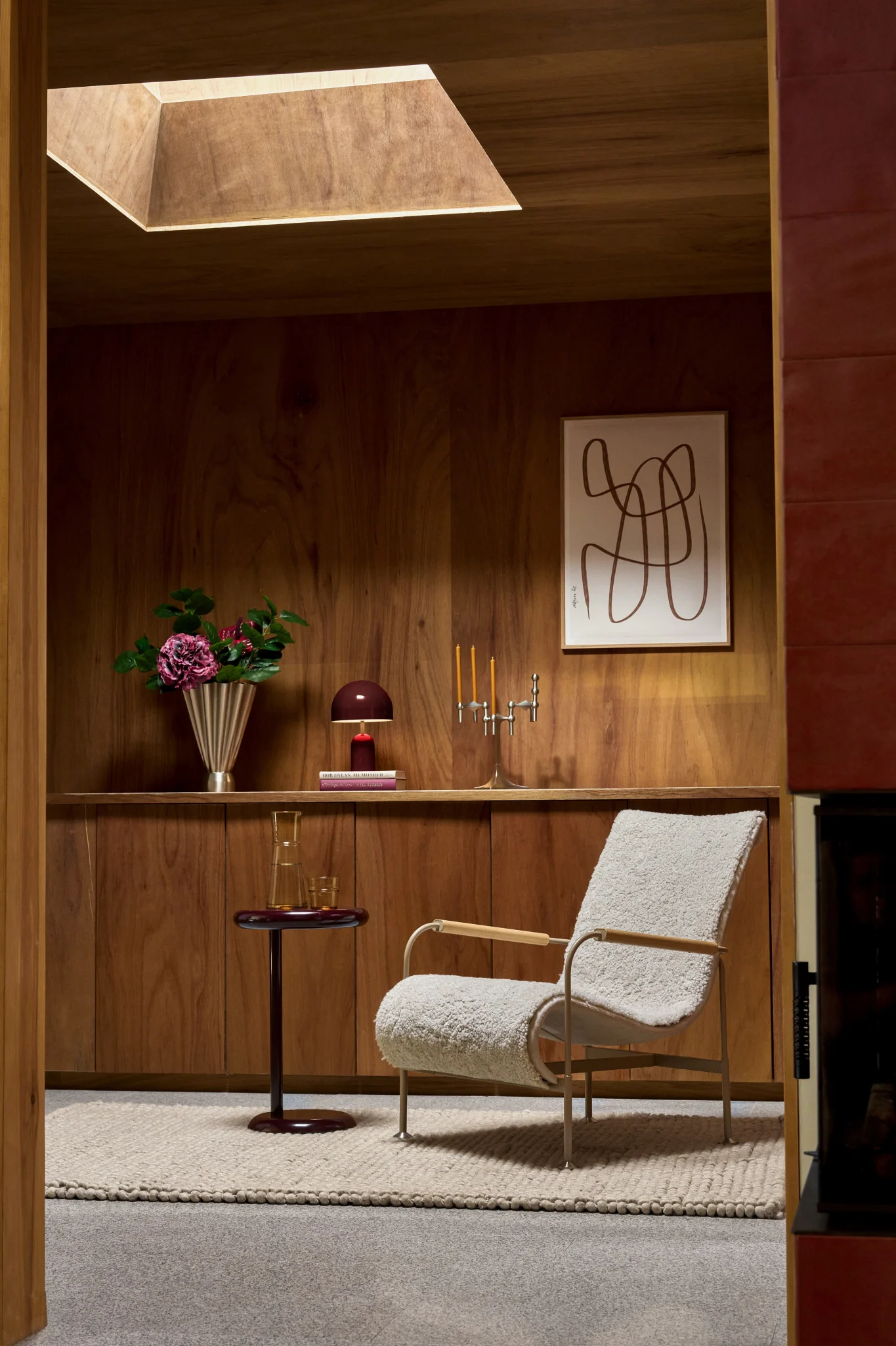 Pièce chaleureuse avec murs en bois, fauteuil bouclé crème, table d'appoint, fleurs et art abstrait.