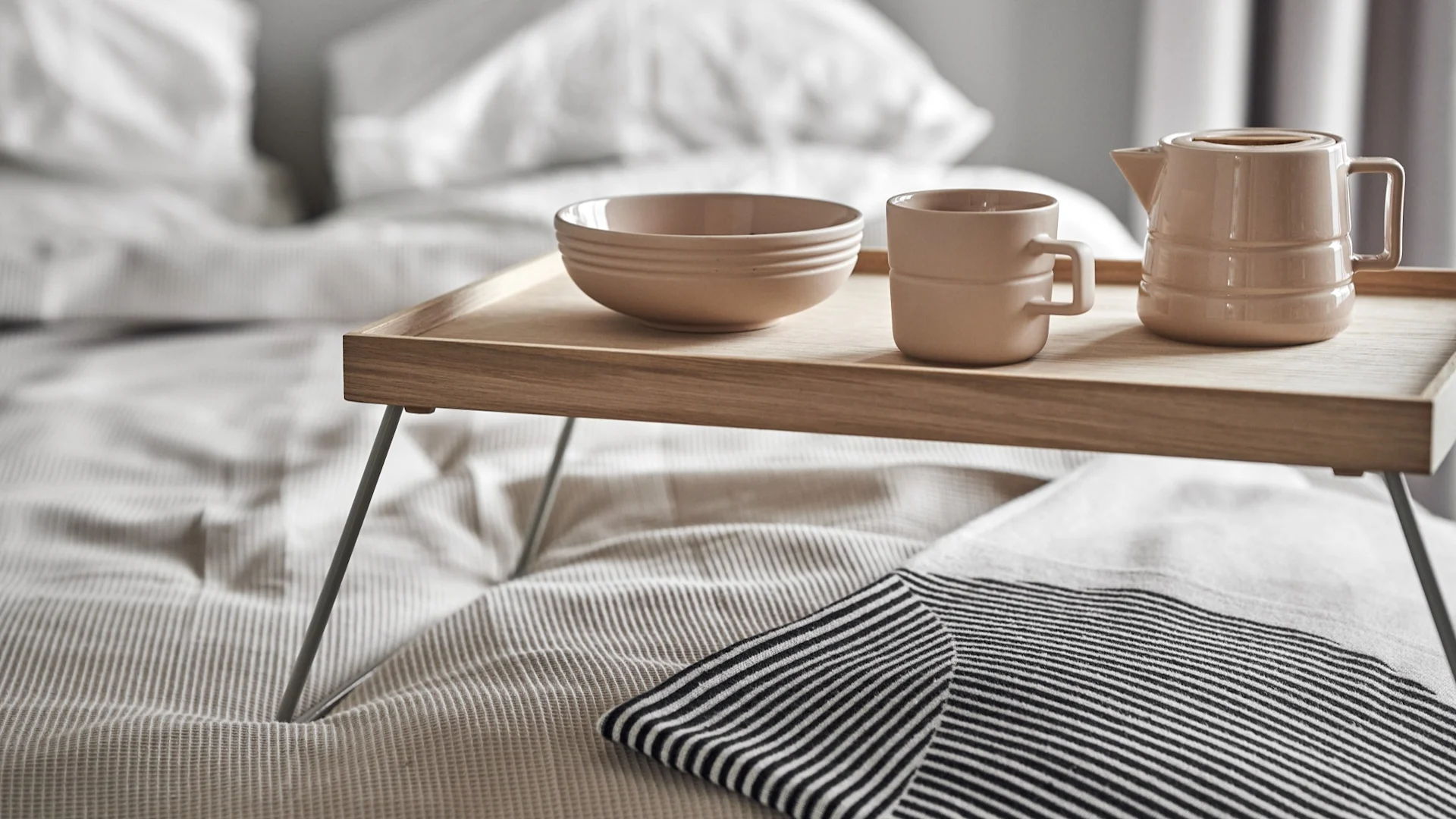 Lagom signifie aussi commencer la journée de manière détendue. Ici, une tasse, un pot et un bol de la collection Lines de NJRD sont posés sur un plateau de petit-déjeuner au lit.