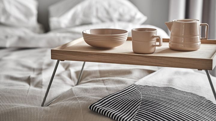 Lagom signifie aussi commencer la journée de manière détendue. Ici, une tasse, un pot et un bol de la collection Lines de NJRD sont posés sur un plateau de petit-déjeuner au lit.