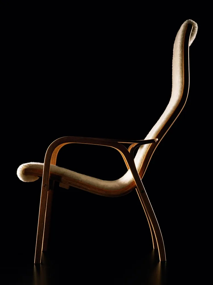 Un élégant fauteuil de salon avec une structure en bois clair courbé et un revêtement en fourrure crème, sur fond noir.
