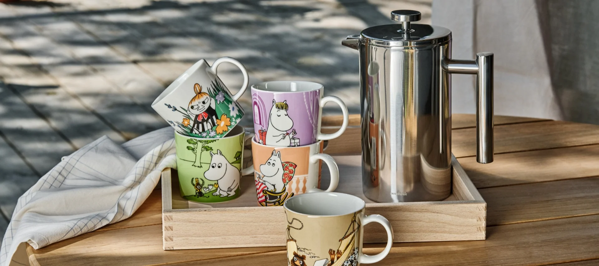 Diverses tasses Moomin de l'Arabie Moomin sont posées sur une table à l'extérieur, à côté d'un pot d'estampage.
