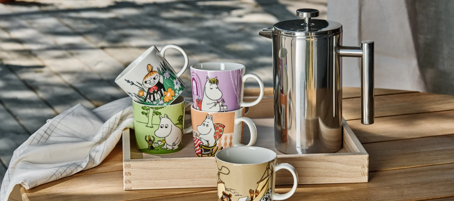 Diverses tasses Moomin de l'Arabie Moomin sont posées sur une table à l'extérieur, à côté d'un pot d'estampage.
