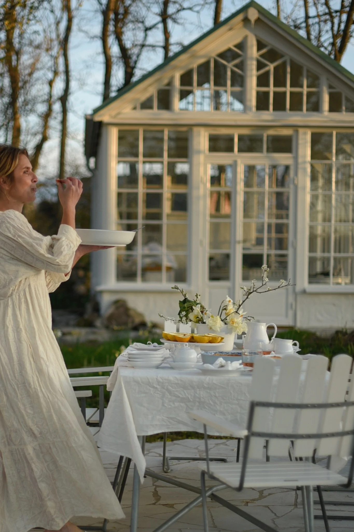 Une table dressée avec des chaises blanches A2 de Grythyttan se trouve devant une serre dans le jardin de @khouri.julia.