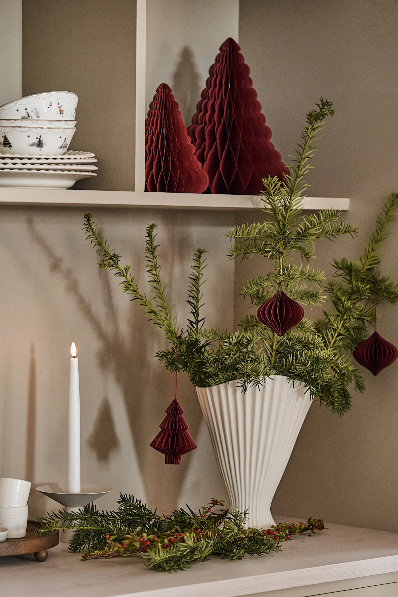 Fabriquer des décorations de Noël avec du sapin : ici, vous pouvez voir des branches de sapin dans le vase Fountain de ferm LIVING, décorées avec des pendentifs de Noël de Scandi Living sur un buffet de cuisine.