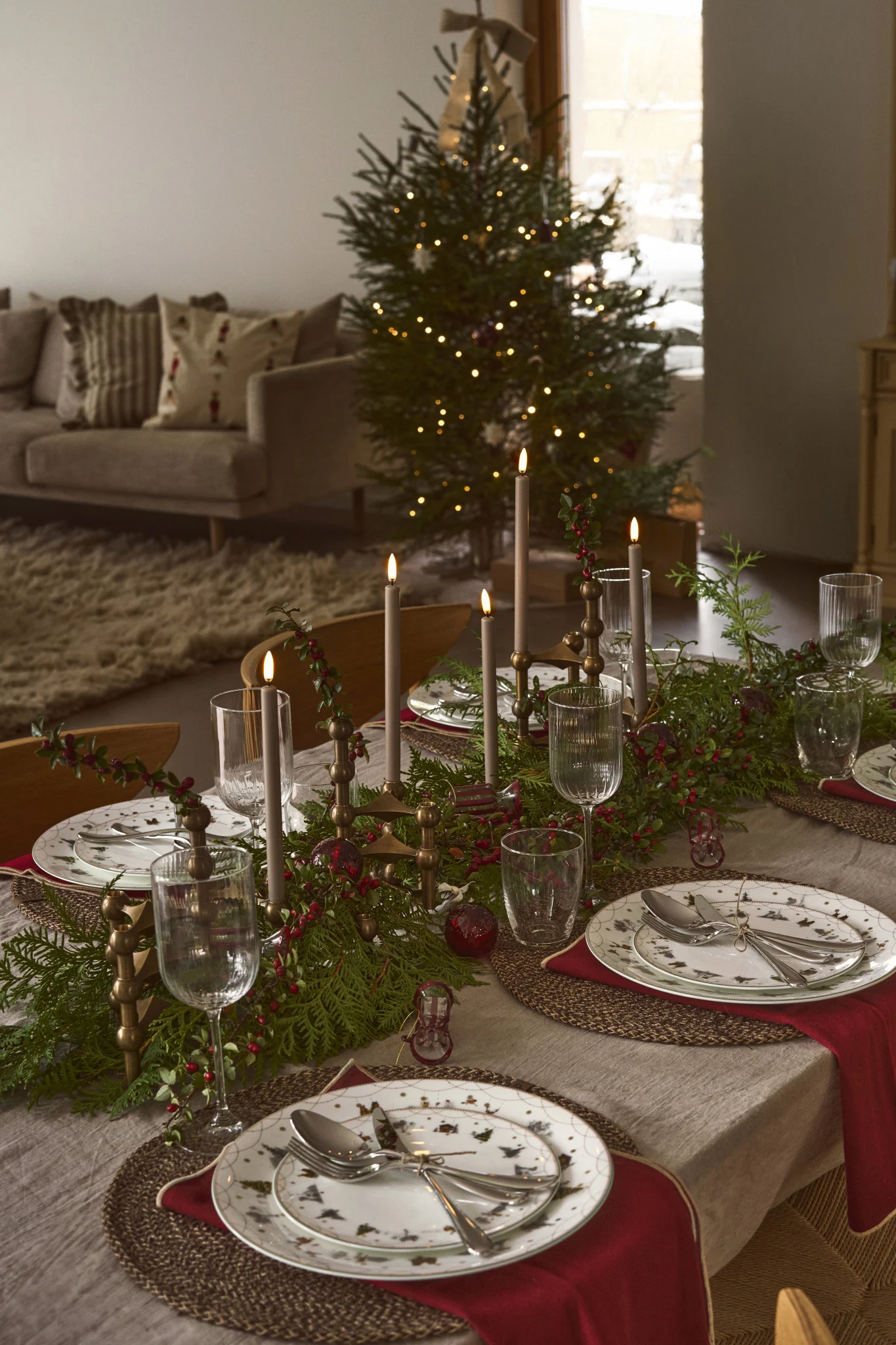 Une table de Noël décorée avec un chandelier de l'Avent comme pièce maîtresse, entouré de branches de sapin et de détails de Noël évocateurs.