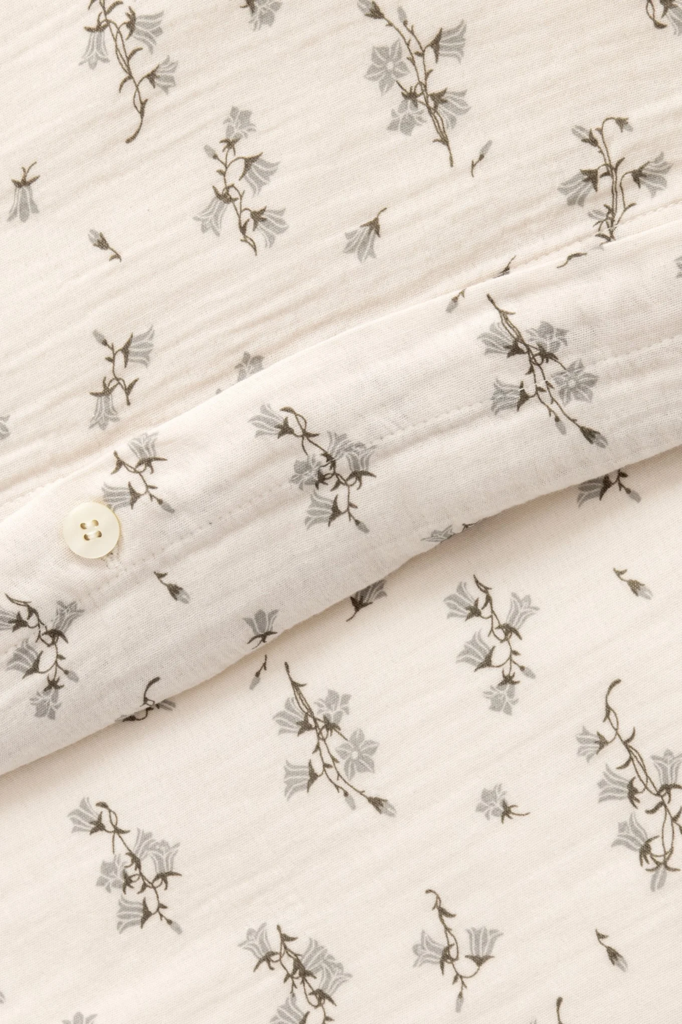Gros plan d'un tissu crème avec un motif de campanules grises et un bouton blanc.