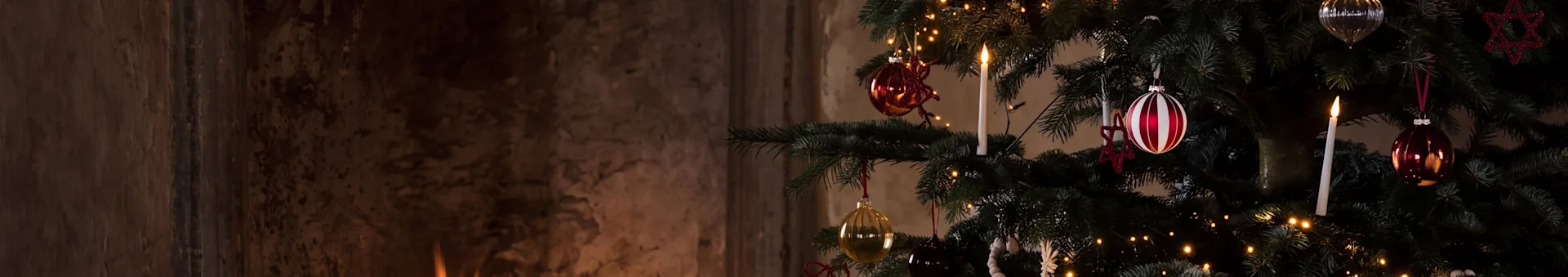 Un sapin de Noël festif avec des ornements et une bougie allumée à côté d'une cheminée chaleureuse avec des bûches qui brûlent.