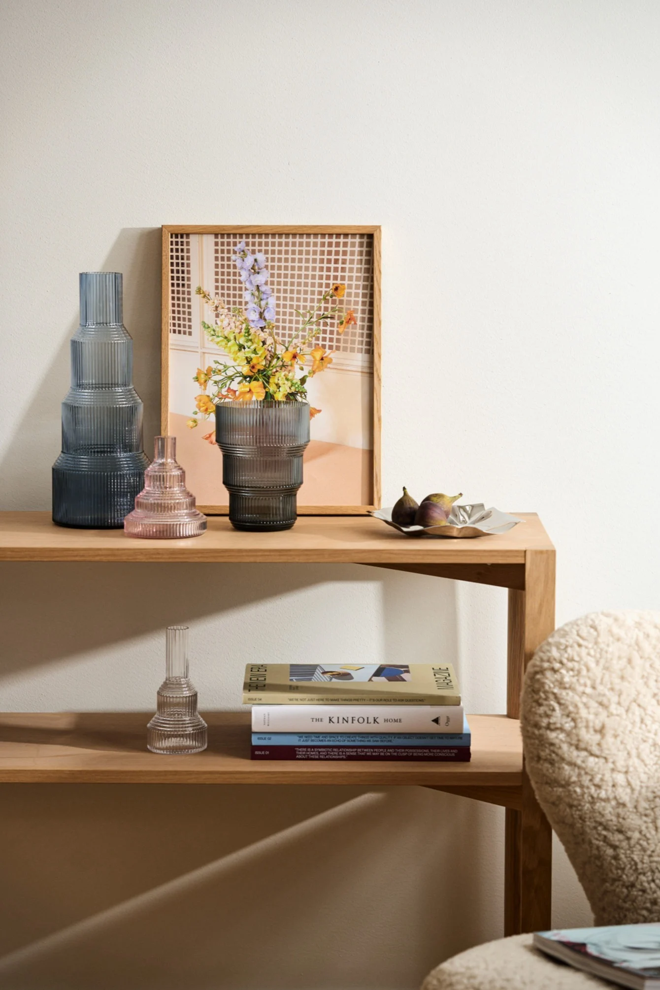 Étagère en bois: trois vases en verre striés (bleu foncé, rose, gris avec fleurs), un cadre, des figues et des livres empilés.