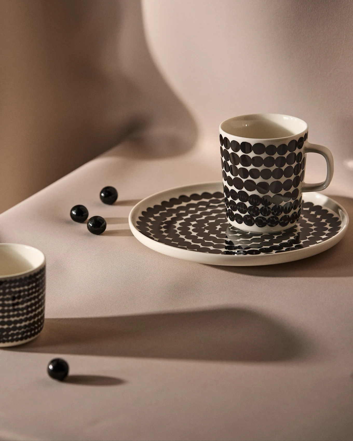 Tasse et soucoupe blanches à pois noirs sur fond neutre, avec des perles décoratives noires éparpillées.