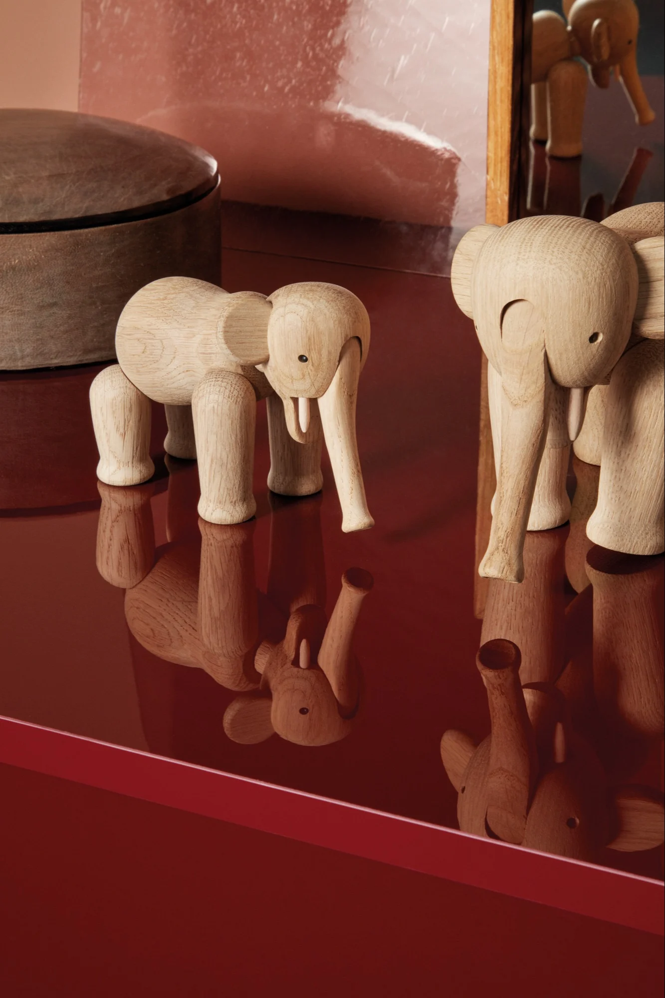 Deux figurines d'éléphants en bois clair posées sur une surface rouge réfléchissante.