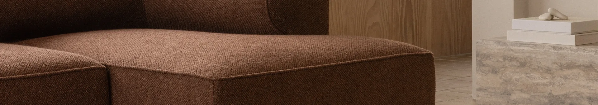 Gros plan d'un canapé marron texturé, mur en bois et objets décoratifs sur béton en arrière-plan.