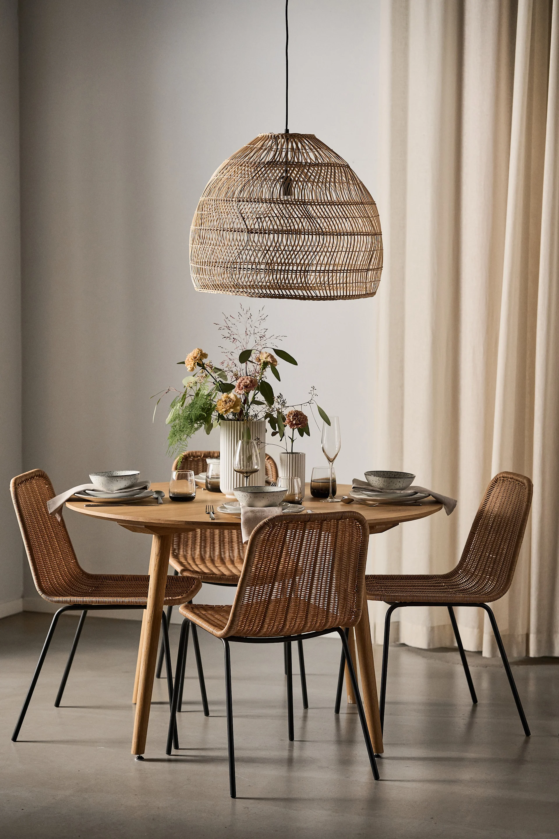 Une salle à manger décorée dans un style bohème avec une lampe en raphia et une table ronde entourée de quatre chaises Hapur de House Doctor.