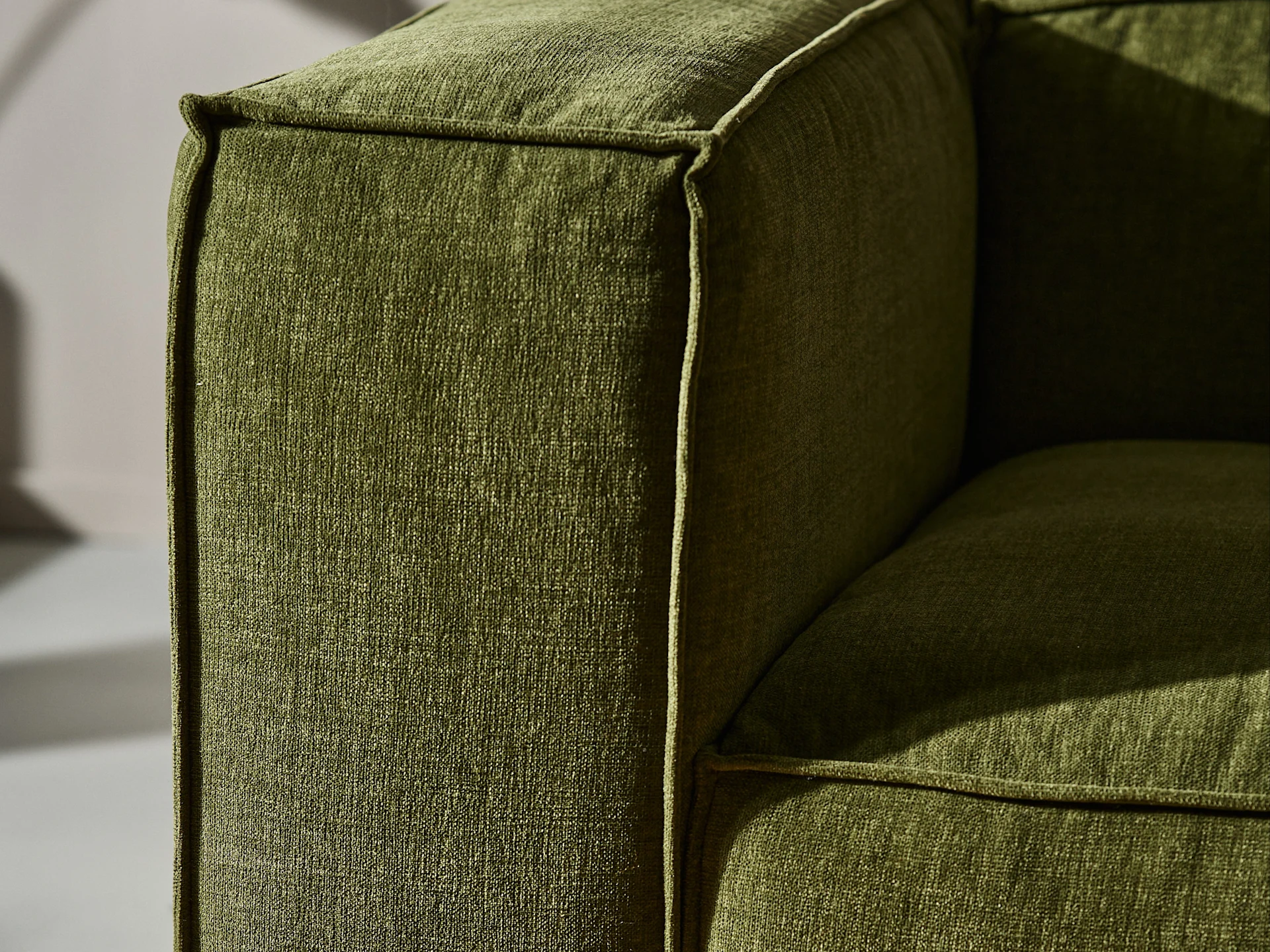 Gros plan d'un accoudoir de canapé en tissu vert avec texture et passepoil visibles.
