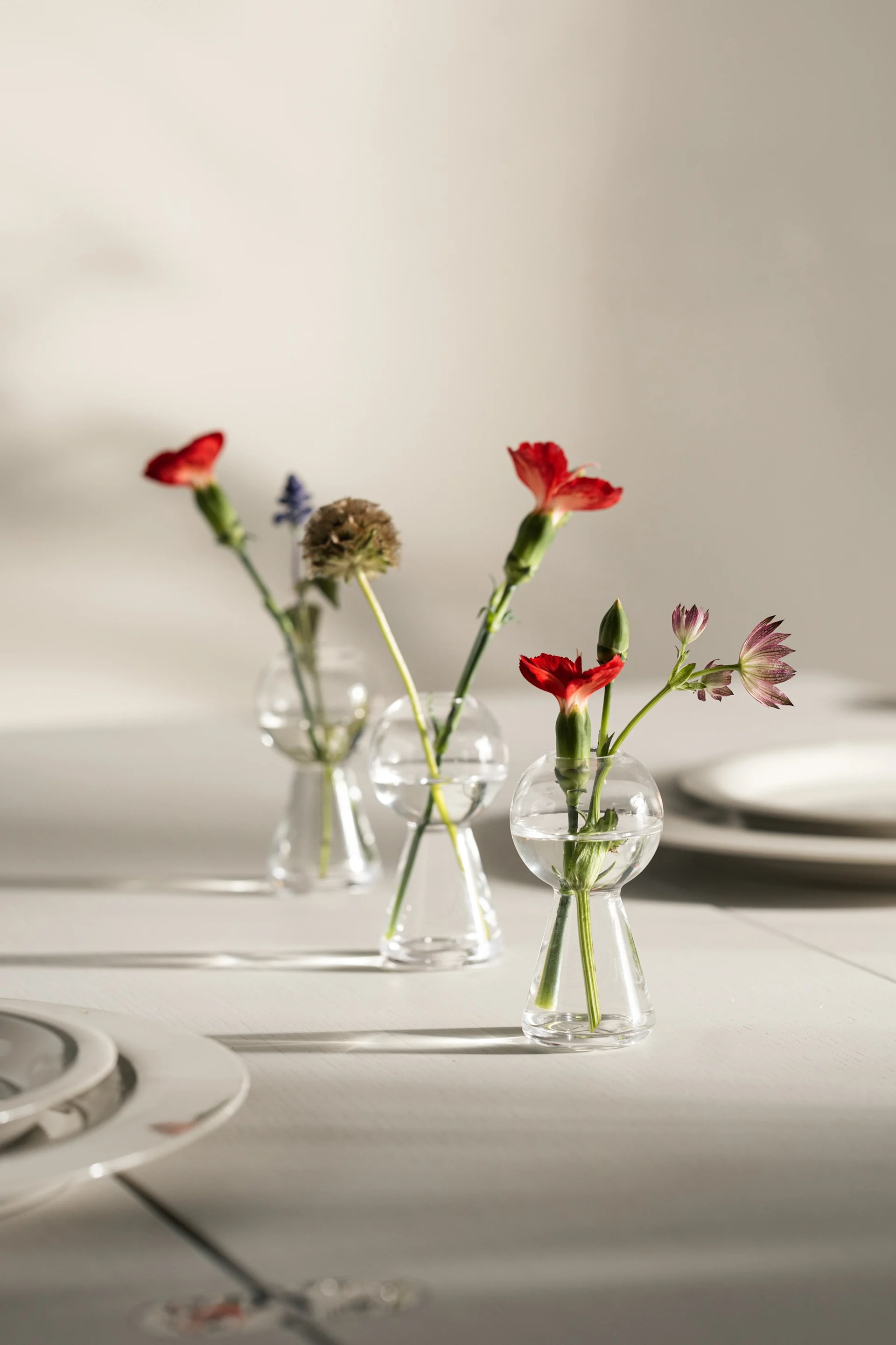 Sur une table dressée se trouvent trois mini-vases contenant chacun une fleur, créés par Design House Stockholm.
