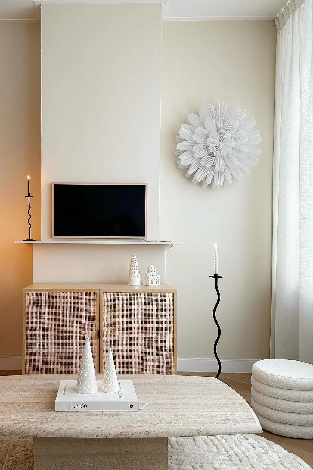 Un salon neutre avec tapis texturé, table basse en travertin, meuble en rotin avec TV, lampadaire et décoration murale plissée.