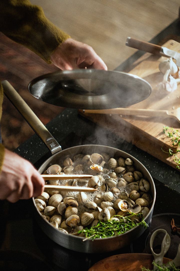 Une personne prépare des moules dans la sauteuse en acier inoxydable Norden Steel de Fiskars.