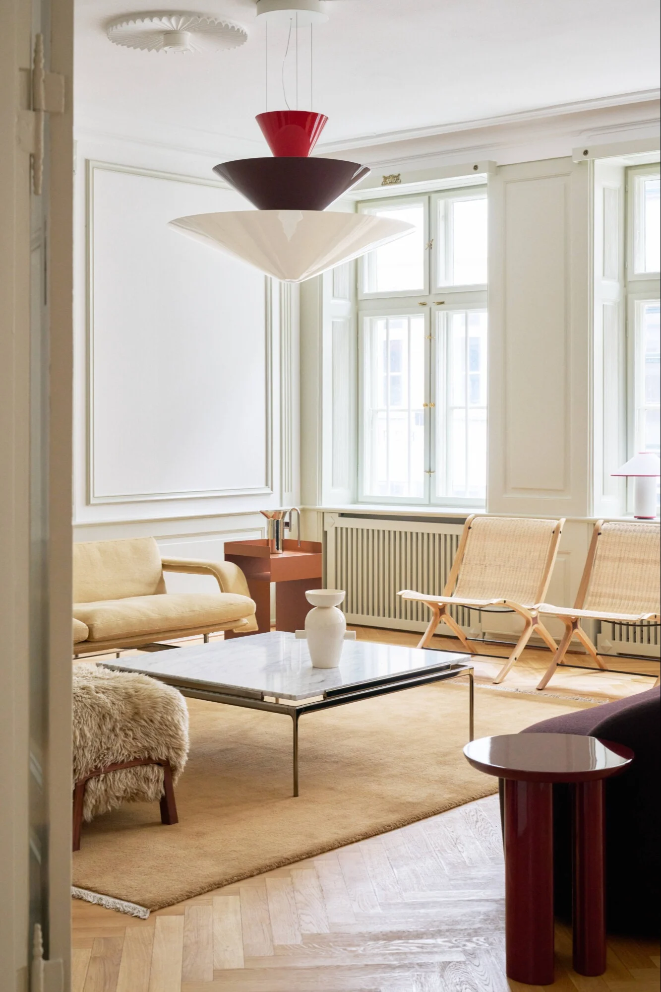 Un salon contemporain avec une suspension à niveaux, un canapé jaune clair, des chaises en rotin et une table basse en marbre.