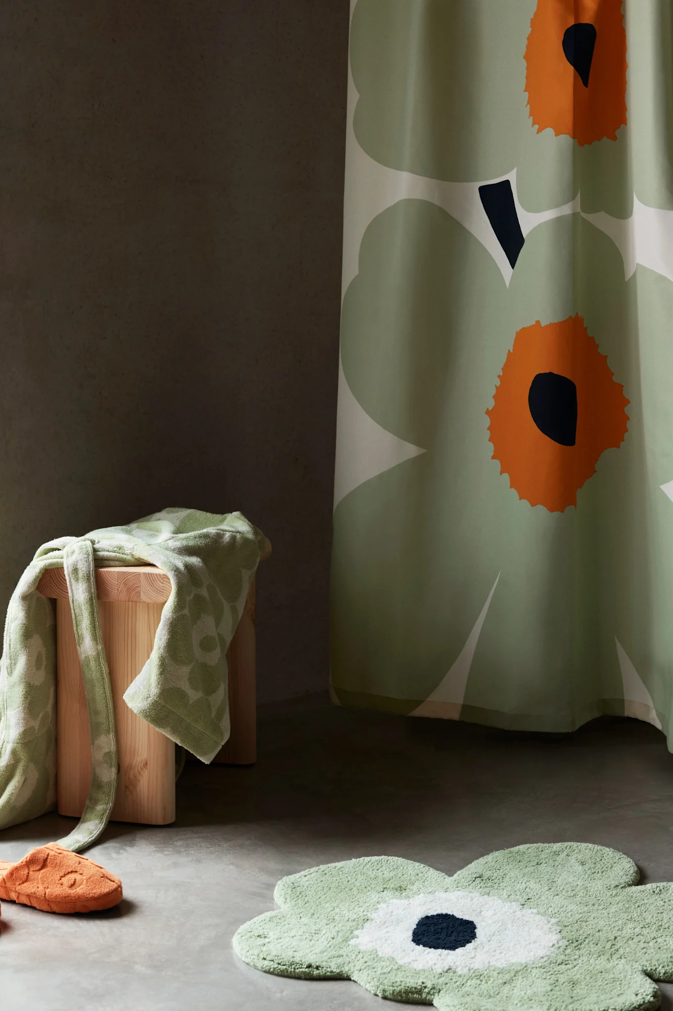 Décor de salle de bain avec rideau de douche floral vert, tapis de bain, serviette sur tabouret et pantoufle orange.