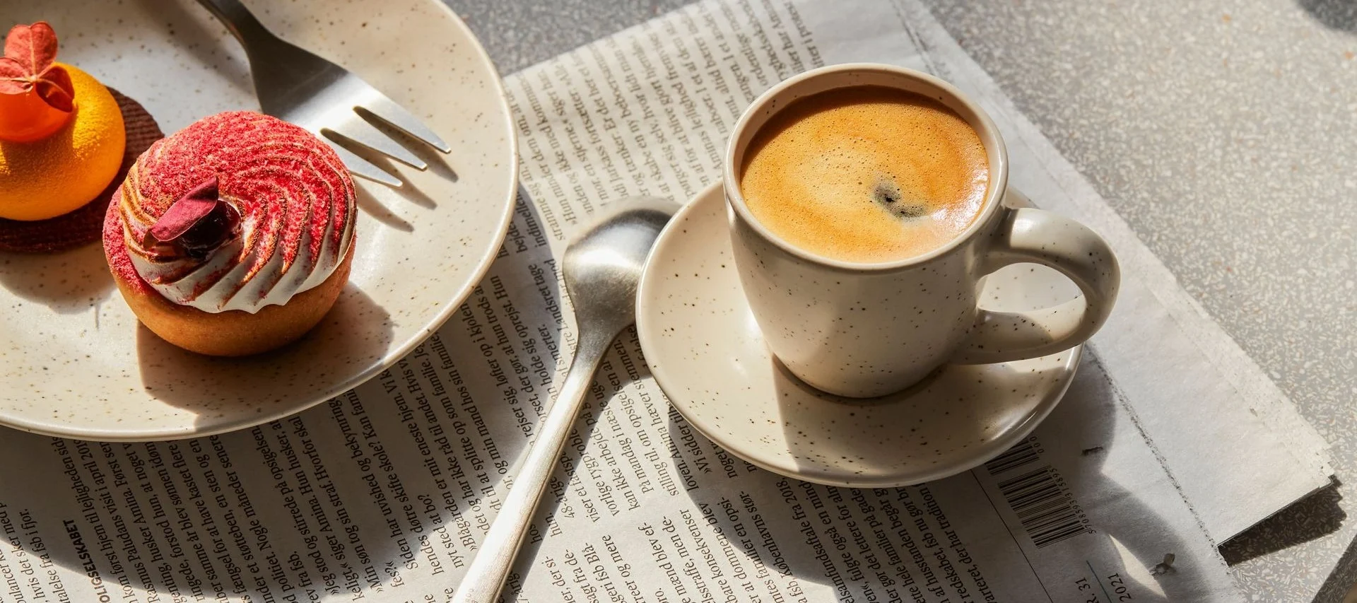 Tasse de café et deux pâtisseries, une tarte rouge et une orange, sur un journal.