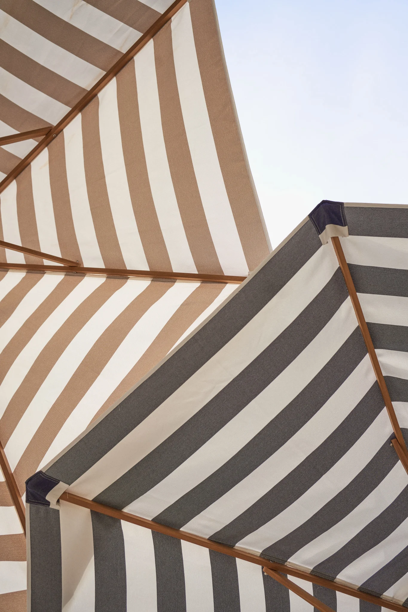 Deux parasols rayés se détachent sur le ciel bleu : l'un est marron et blanc, l'autre gris et blanc.