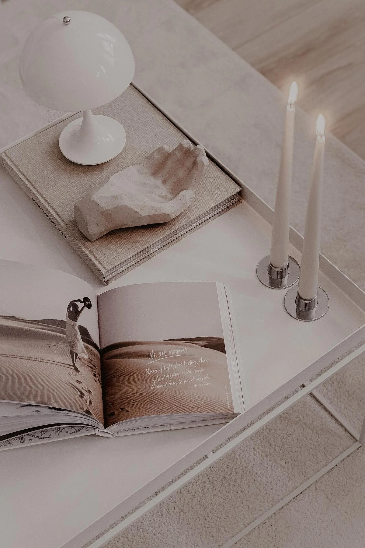 Une grande table basse, décorée avec des livres, une main décorative, deux bougies et une lampe de table Panthella portable de Louis Poulsen.