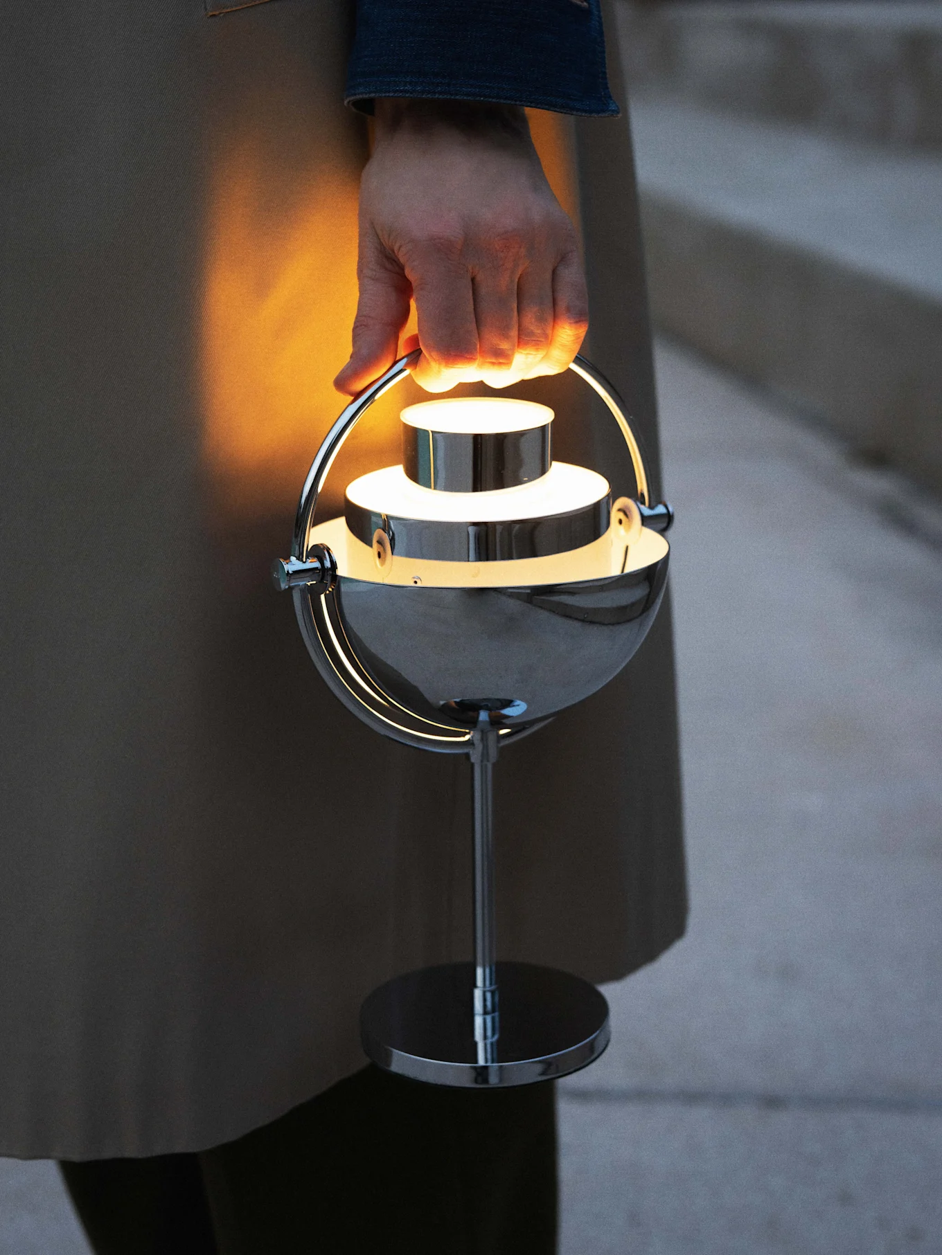 Main tenant une lampe portable chromée, moderne et lumineuse.