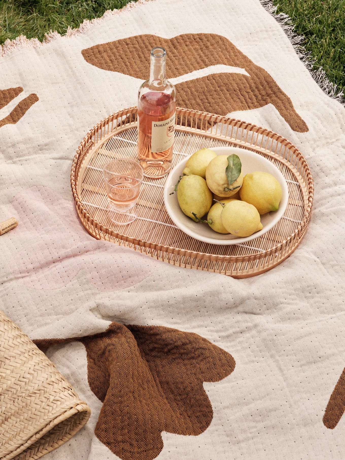Couverture de pique-nique sur l'herbe avec plateau en rotin, vin rosé, verre et un bol de citrons.