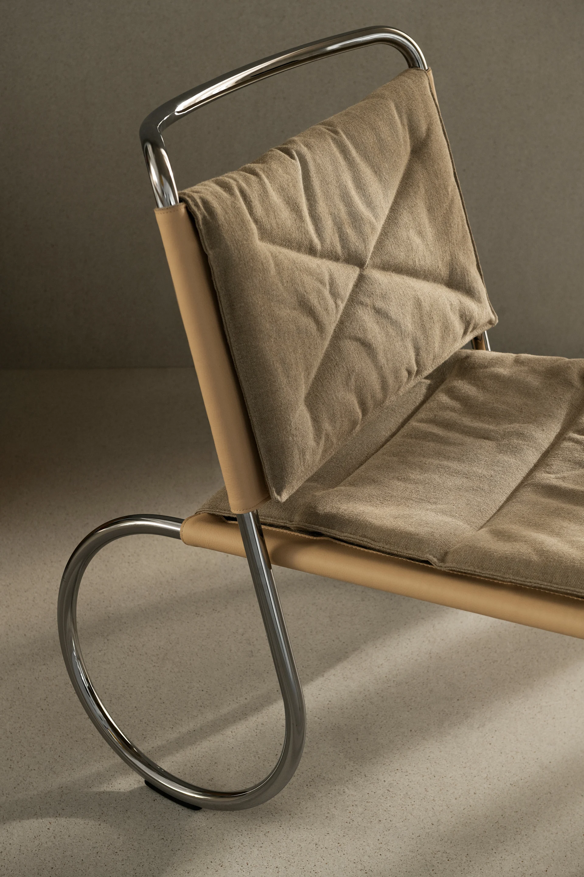Gros plan sur une chaise moderne dotée d'une structure en chrome poli, d'une assise en cuir beige clair et de coussins en tissu beige matelassé.