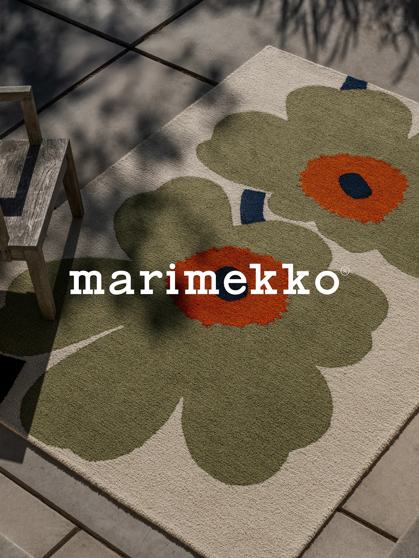 Tapis Marimekko avec grand motif floral vert et orange sur une terrasse avec une chaise en bois.