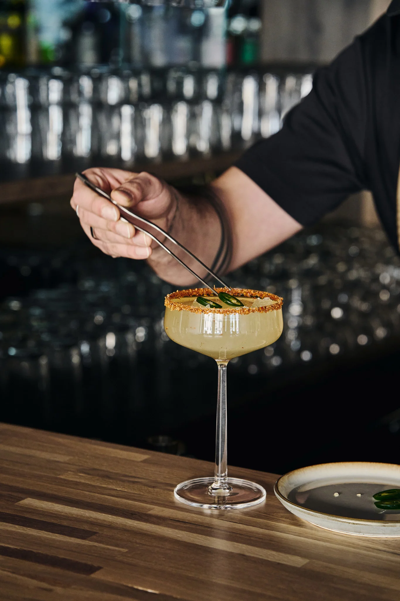 Parfait pour les cocktails sans alcool : le verre à cocktail Essence d'Iittala avec boisson, bord décoré et garni de tranches de jalapeño à l'aide d'une pince.