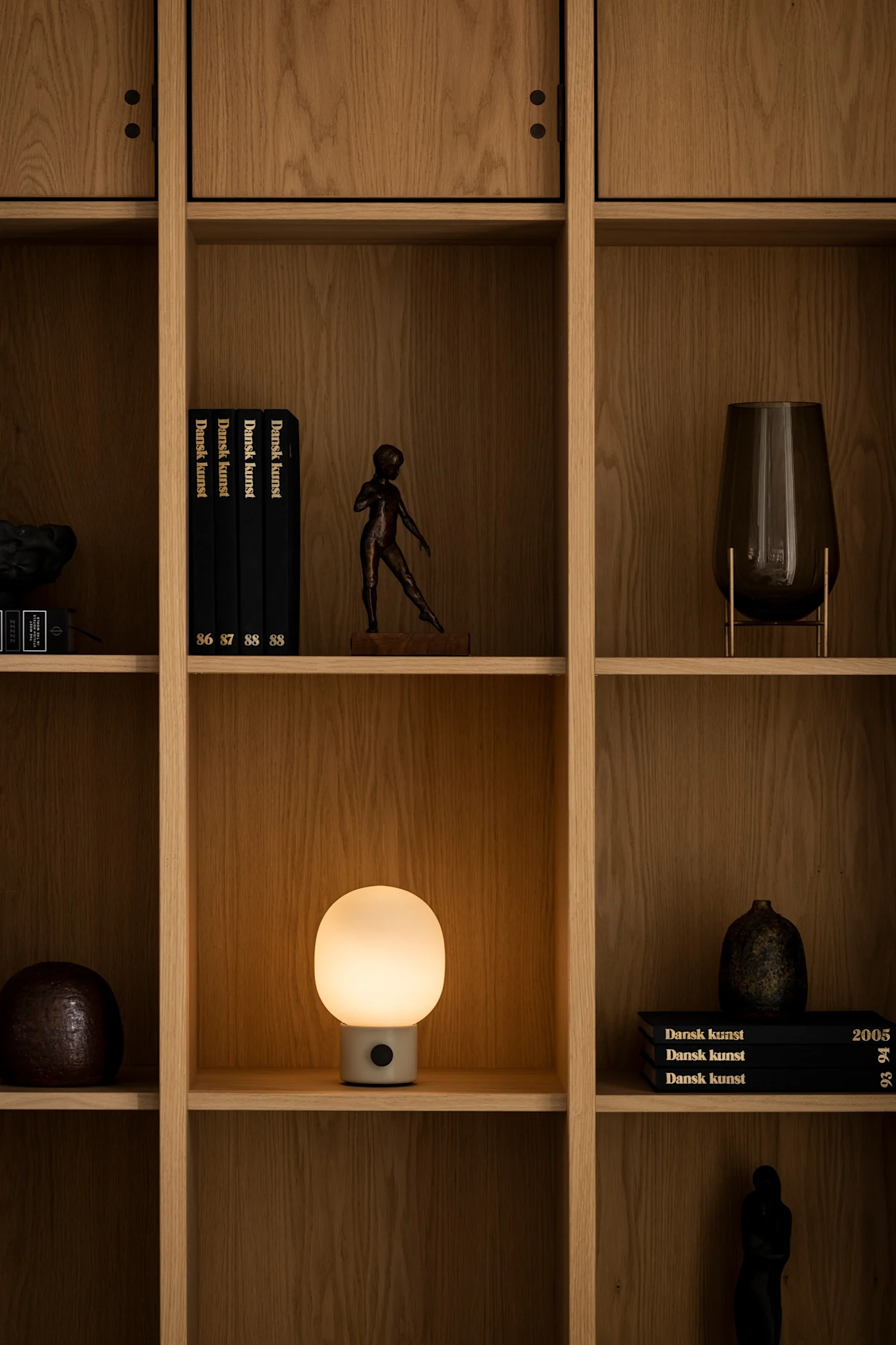 La lampe rechargeable JWDA d'Audo Copenhagen est posée sur une étagère et éclaire la pièce avec d'autres décorations. 