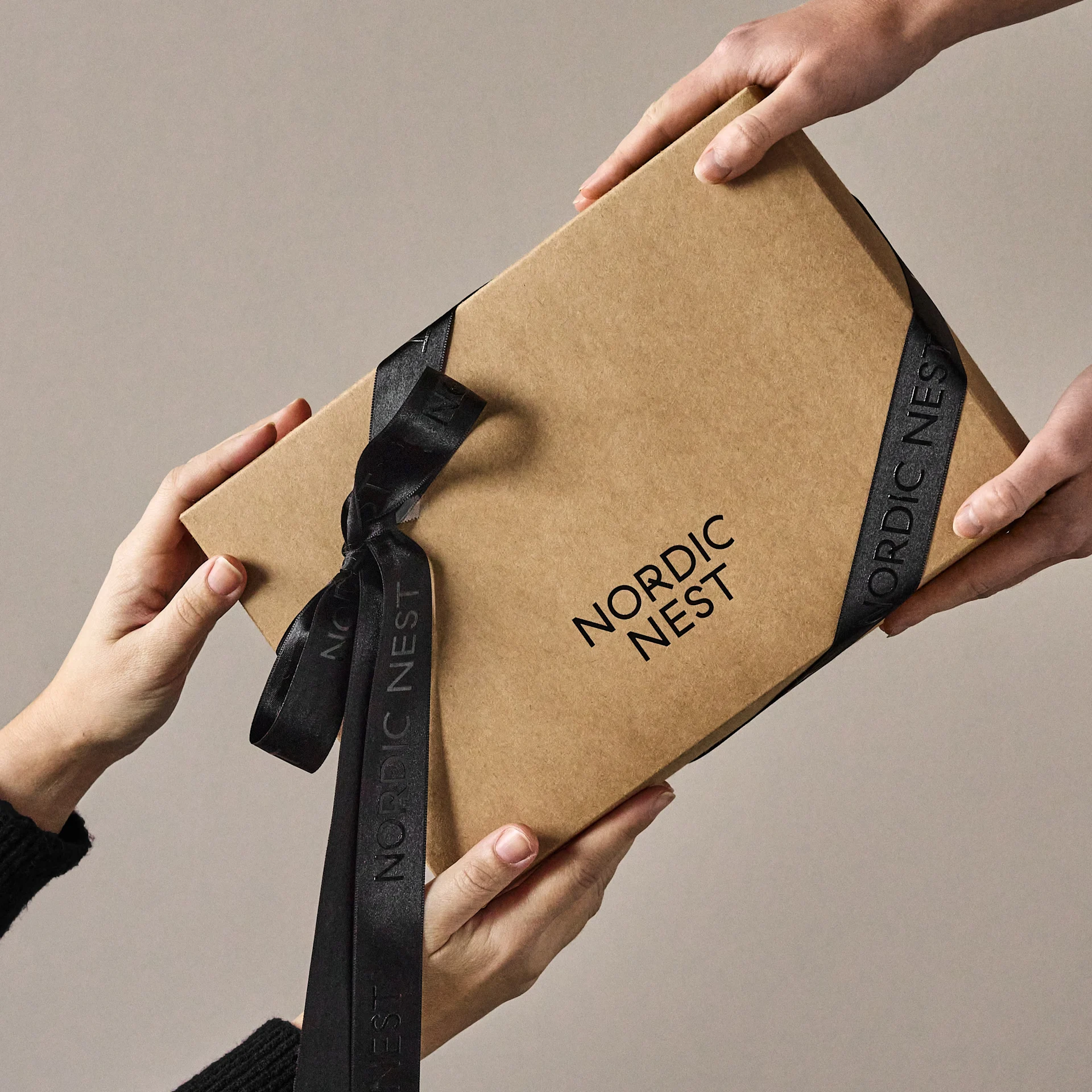 Mains échangeant une boîte cadeau marron avec le logo 'Nordic Nest' et un ruban noir.