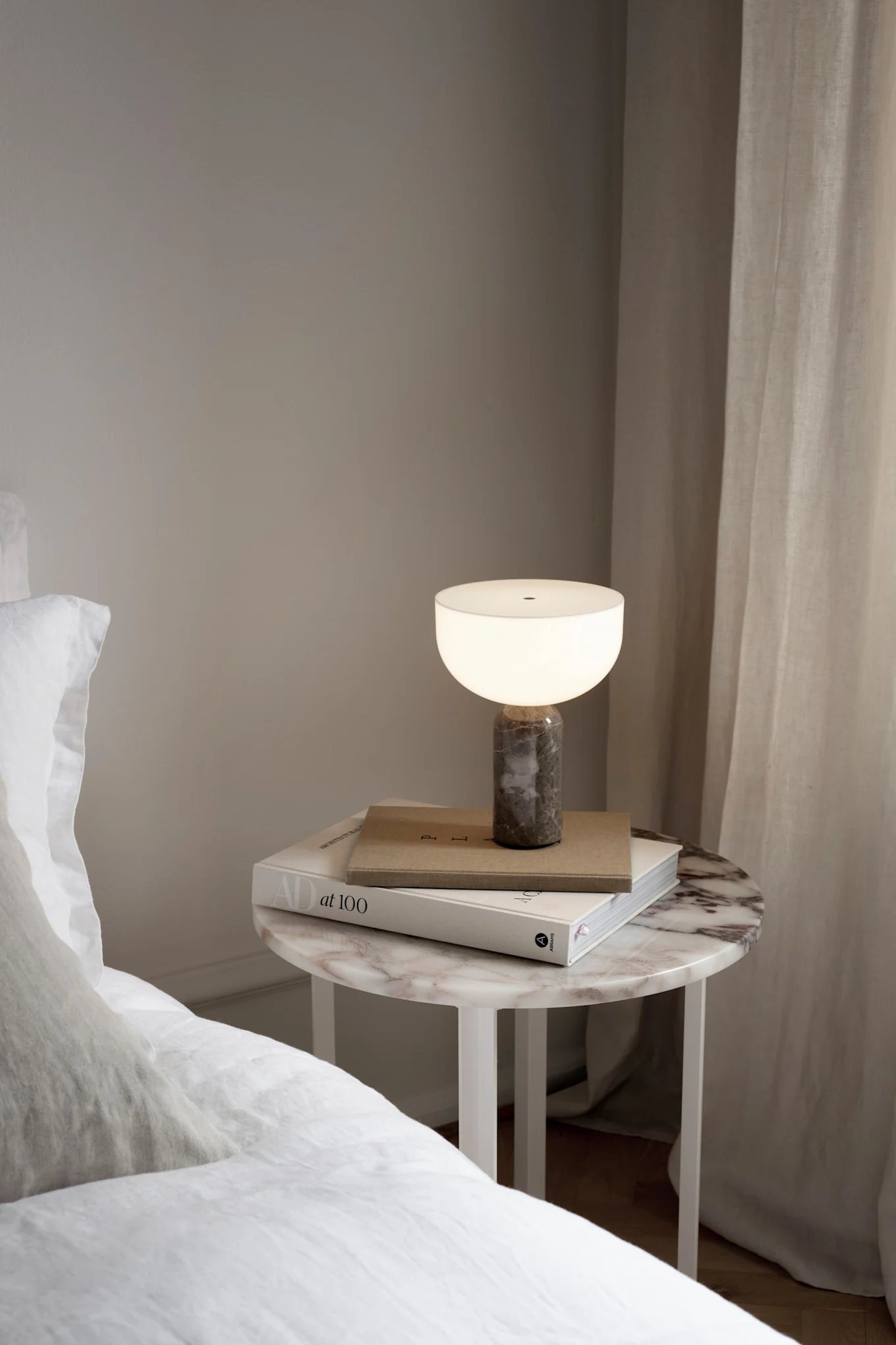 La lampe rechargeable Kizu est posée sur une table de chevet à côté d'un lit.