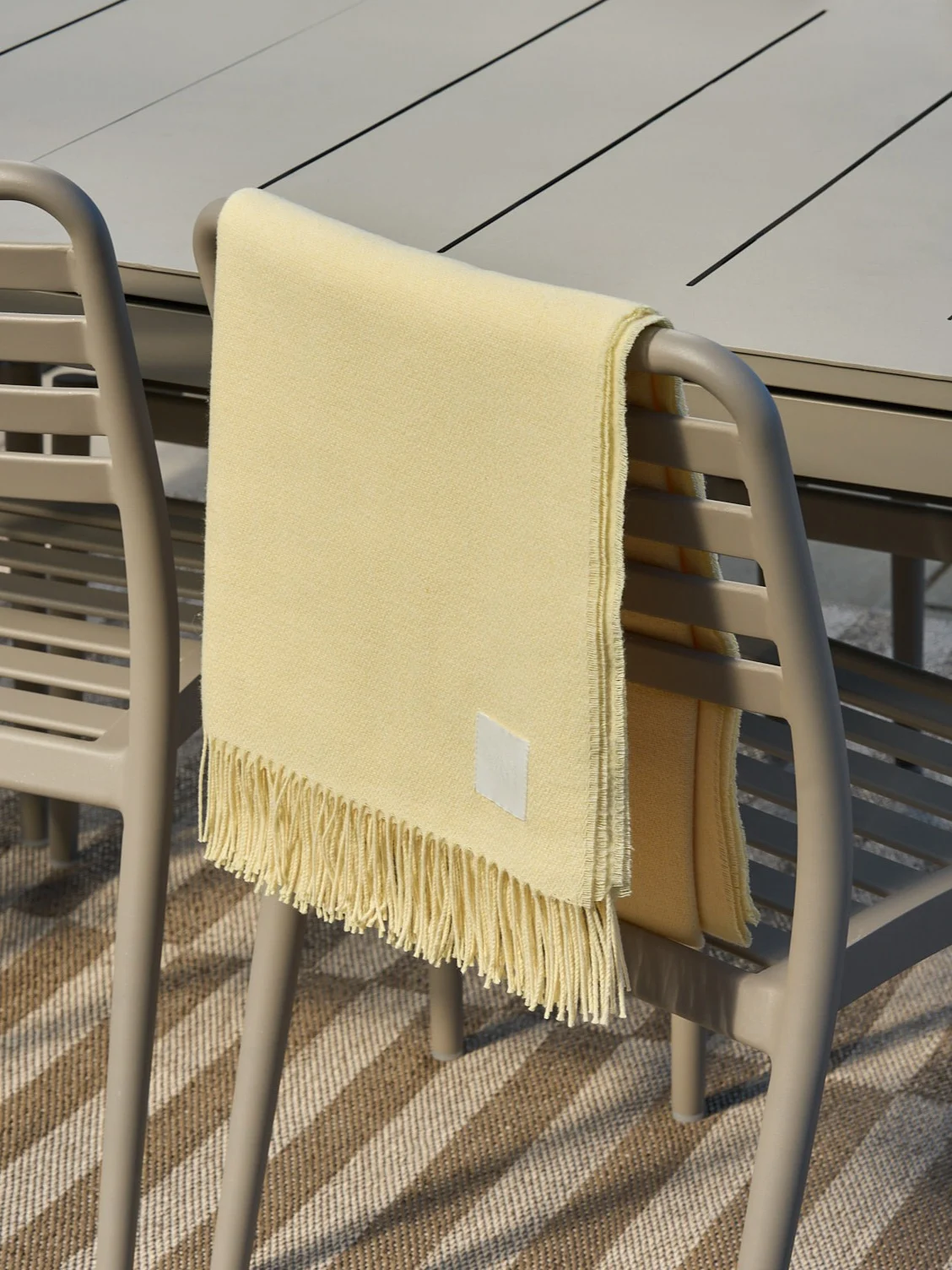 Plaid jaune clair à franges drapé sur une chaise d'extérieur beige.